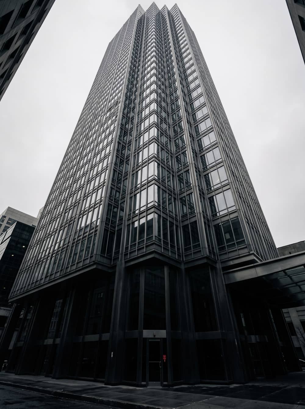 A modern glass and steel tower photographed from street level, its facade receding upward into an overcast sky.
